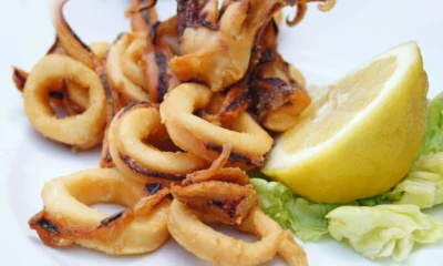 Golden fried calamariere served on a white plate with lemon wedges