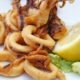 Golden fried calamariere served on a white plate with lemon wedges